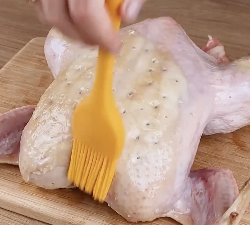 Whole chicken being brushed with oil